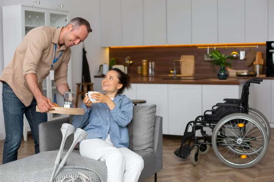 A support worker and a woman using a mobility aid chatting warmly in a bright living room