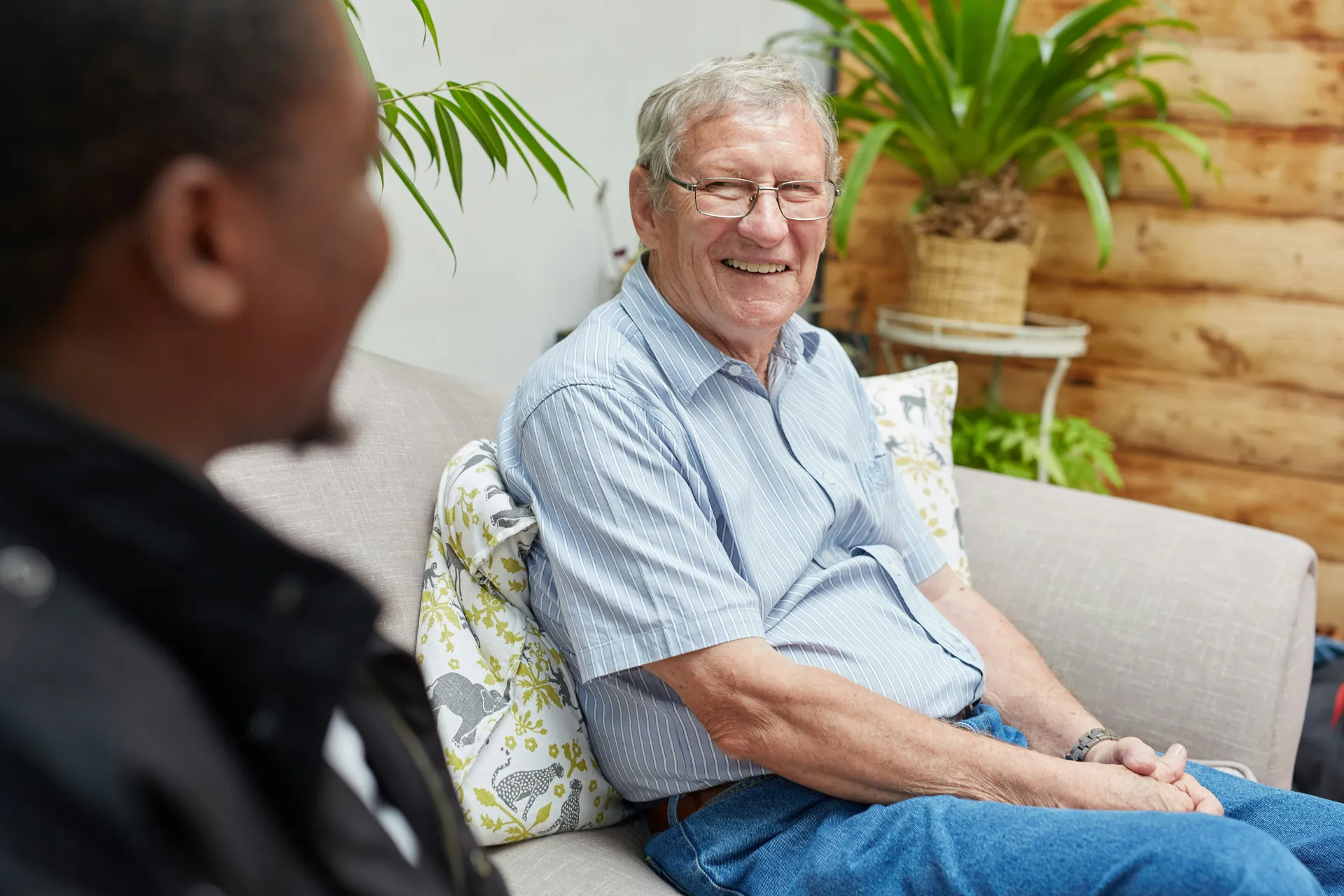 An older man smiling during a relaxed conversation with a support worker on a couch at home