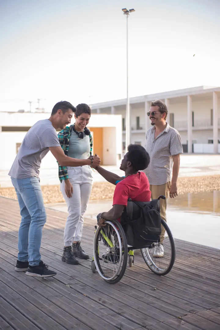 Friends warmly greeting a man using a wheelchair outdoors