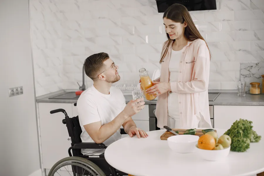 A man using a wheelchair sharing a drink with his partner in a sunny kitchen