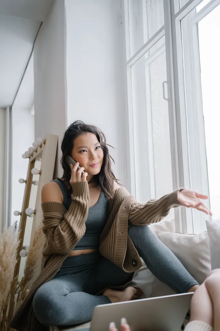 A relaxed woman chatting warmly on the phone by a sunny window at home